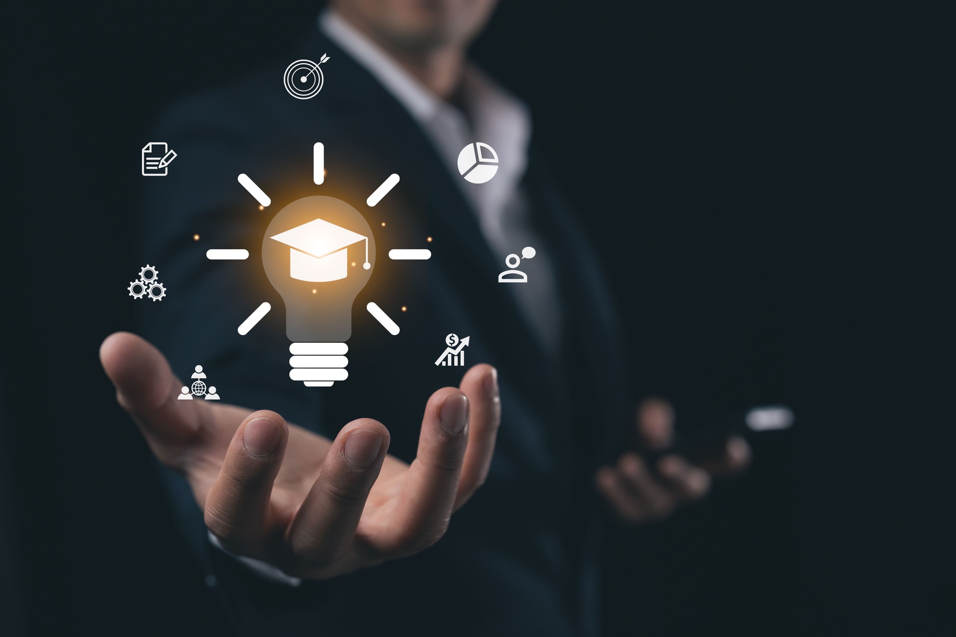 Business Professional Holding Light Bulb with Graduation Cap Icon, Symbolizing Ideas, Innovation, Success, and Education in Modern Corporate Environment